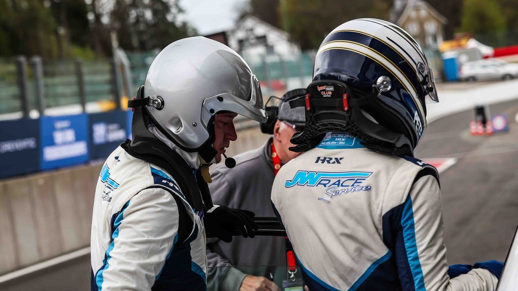 Twee coureurs met helm in overleg bij de auto, drivers helping drivers